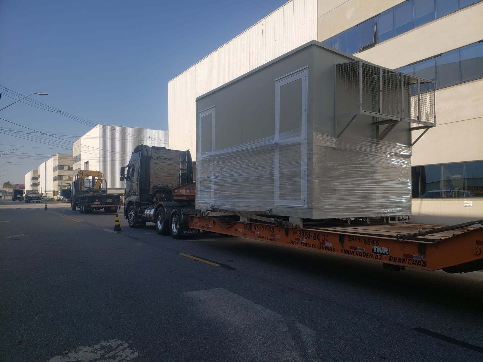 Caminhão com prancha transportando carga indivisível de grande porte em área industrial.