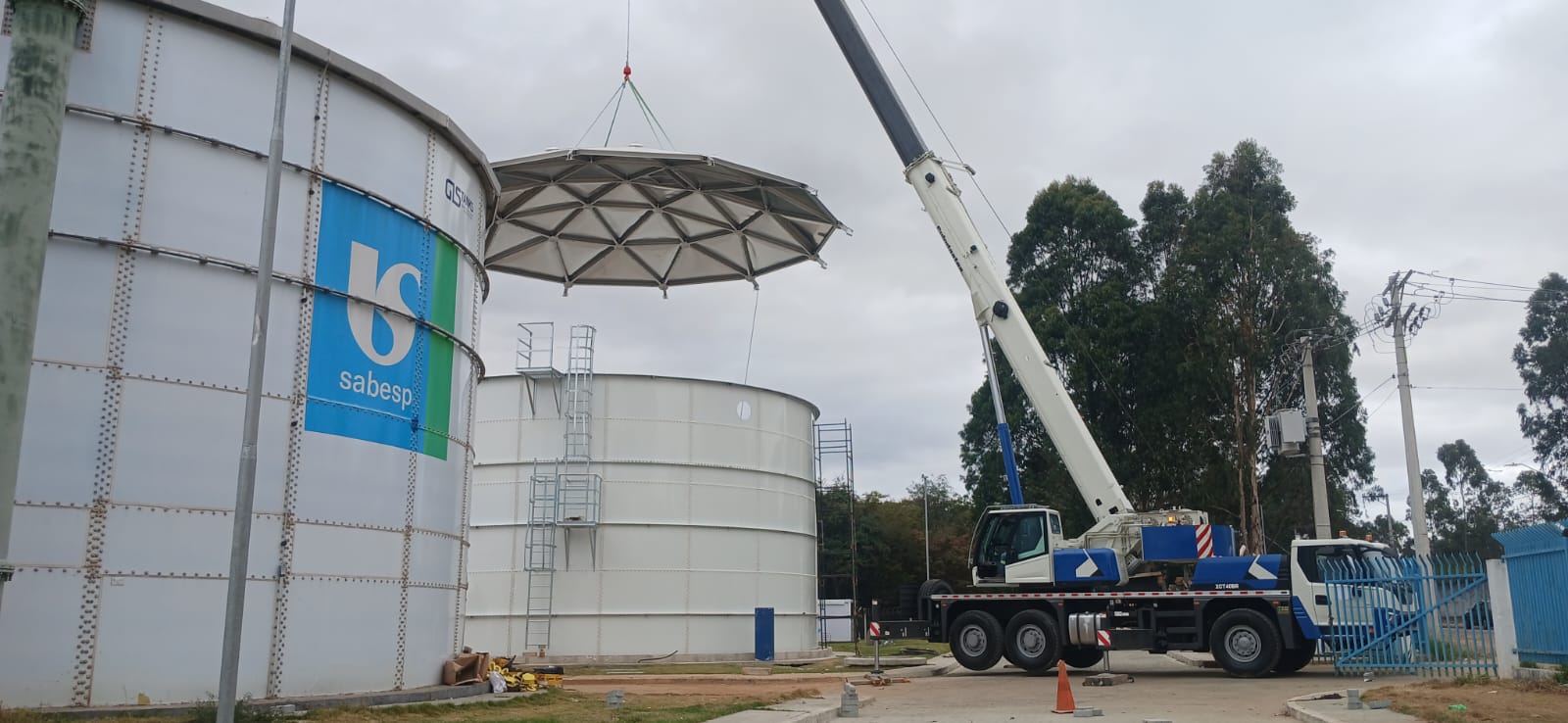 Guindaste içando cobertura metálica de reservatório de água.